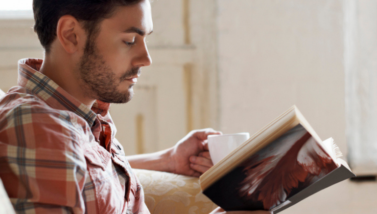 man reading book with cup of tea