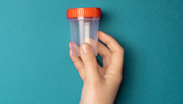 Hand holding up empty fluid sample container against light blue background