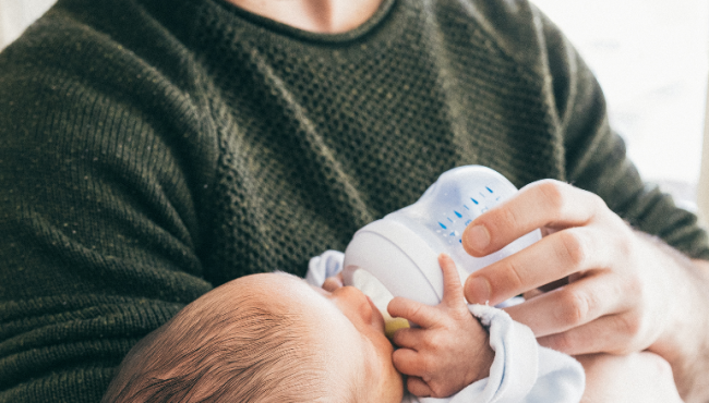 Man in green knit sweater feeding baby bottle of milk