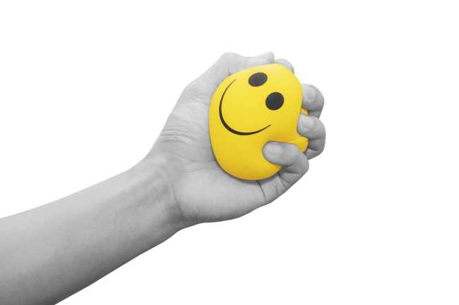hand squeezing a stress ball with a smiley face on it